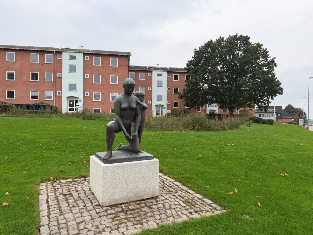 Boligblokke i baggrunden og statue i forgrunden af kvinde med barn