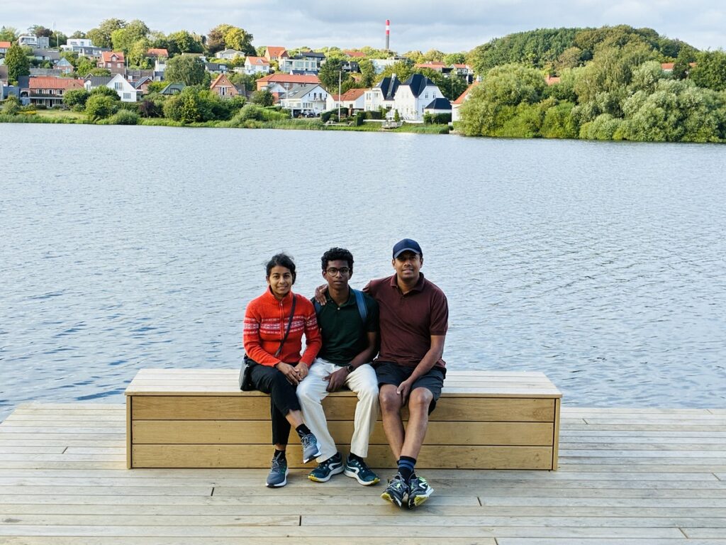Familien fra Sri Lanka sidder på en bænk på Søterassen i Kolding med Slotssøen i baggrunden